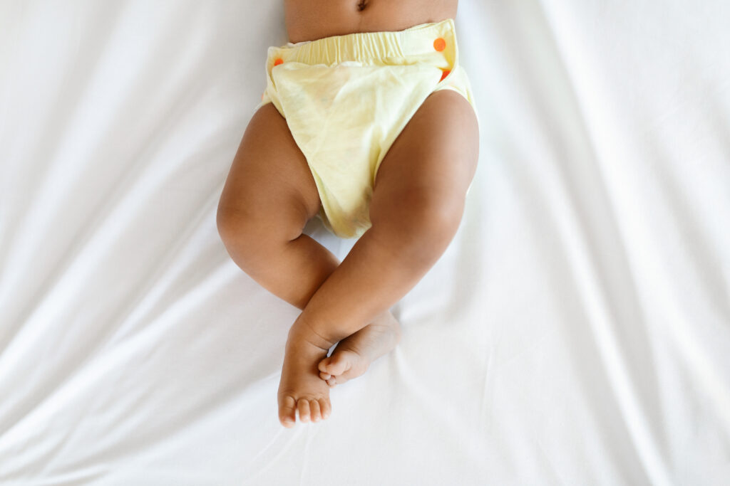 Bottom Part Of Black Infant Baby Wearing Reusable Diaper Lying On Bed baby in underwear