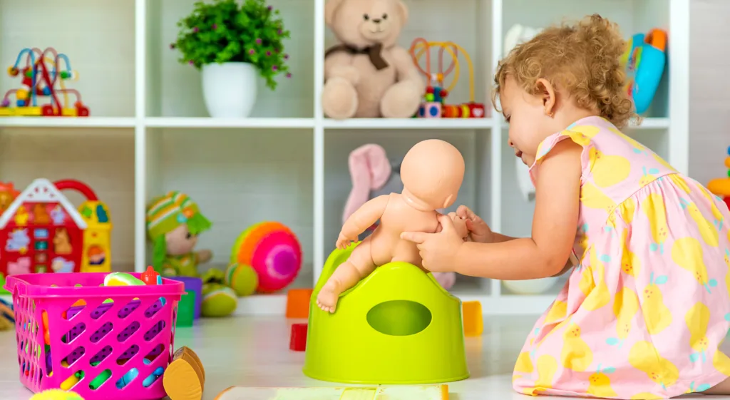 Child playing with her dolls, pretending to make it sit on the toilet seat