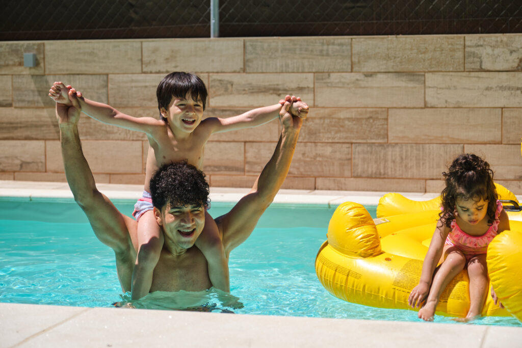 A man with his son on his shoulders near his daughter in a pool A man with his children enjoying summer