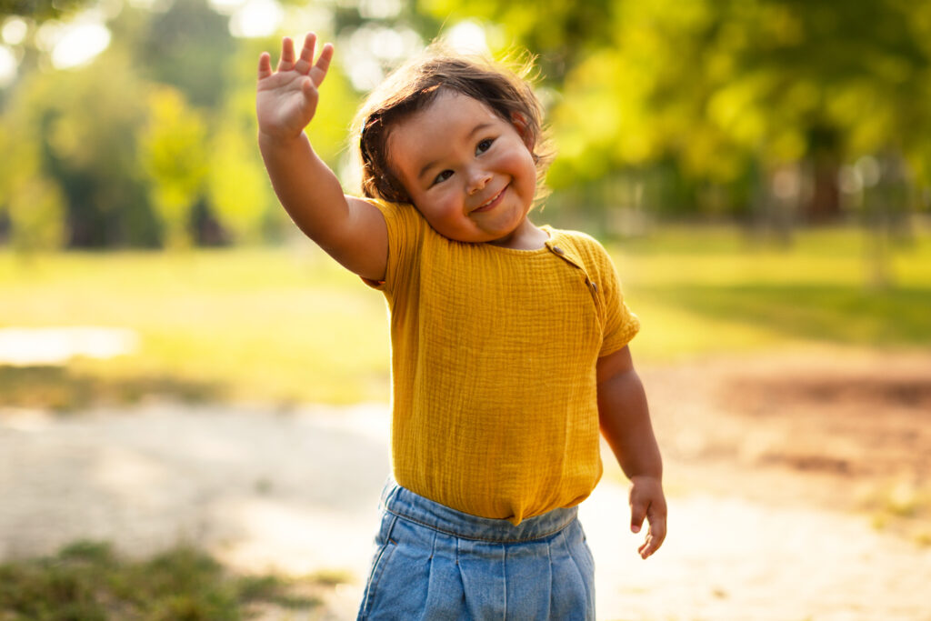 Adorable Little Baby Girl In Casual Waving Hand Standing Outdoor young child waving bye