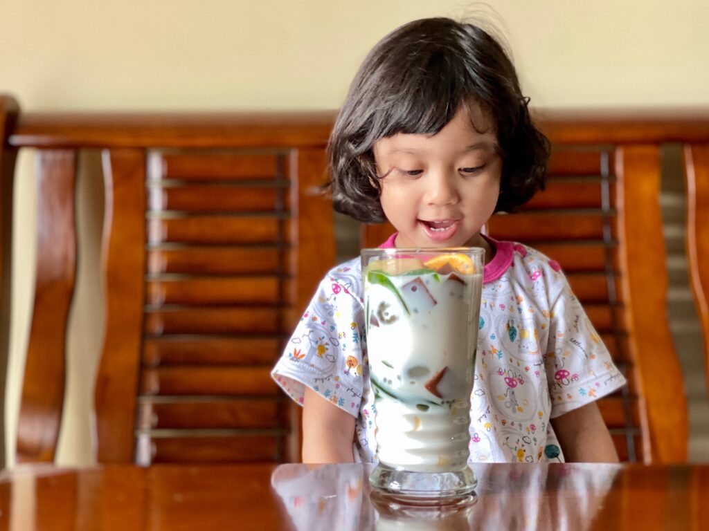 child-with-colorful-iced-drink-sitting-on-wooden-c-2024-12-02-01-33-41-utc child looking excitedly at a cool drink