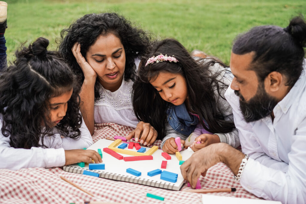 Happy indian family having fun playing with children outdoor at city park - Focus on mother face family enjoying a game together away from the phone
