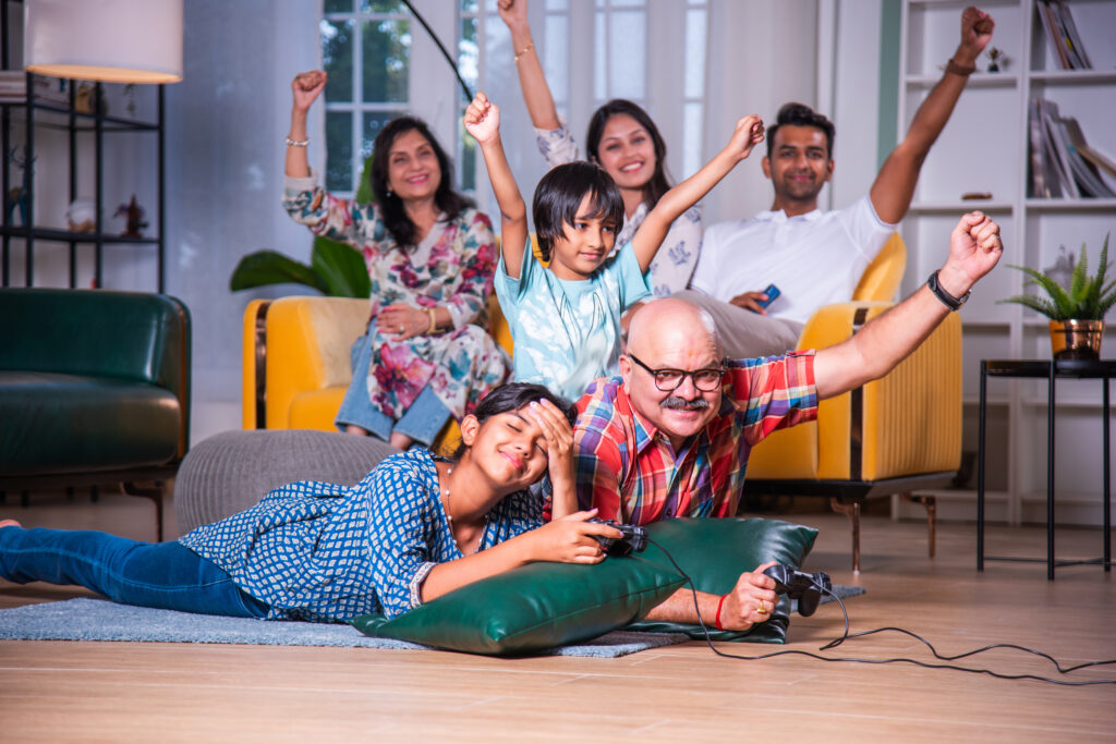 Indian asian Little girl or boy with grandfather playing video game lying on floor at home using joystick and family cheering them
