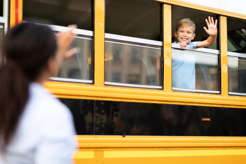 boy waving bye to his mother as he leaves in school bus