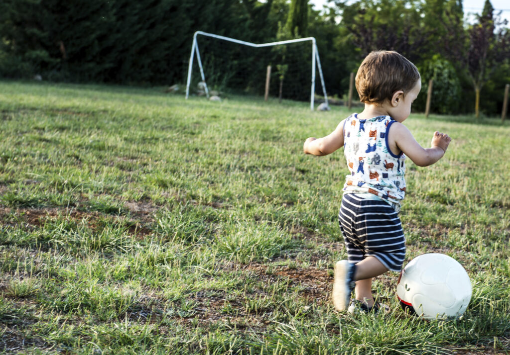 Toddler playing football in park child trying to kick a ball